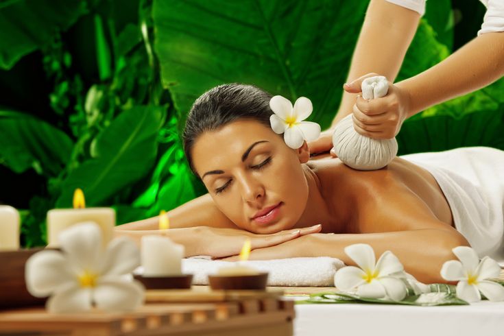 Woman receiving herbal compress therapy massage with plumeria flowers and candles against tropical green backdrop at Holistic Luxury Spa & Salon, Bhopal